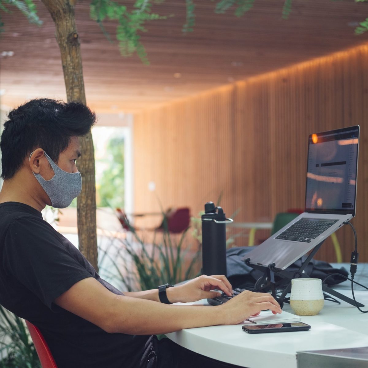 work from home, young man with protective mask on his face working remotely with his laptop